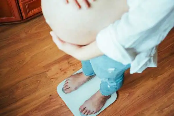 Image of woman weighing herself and experiencing weight gain through pregnancy Clacton